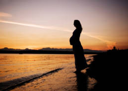 silhouette of pregnant woman standing on the beach at discovery park in Seattle Washington at sunset