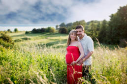 pregnant couple stands together in grassy field