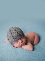 baby wearing a grey hand knit fair isle style fisherman's hat asleep on blue blanket