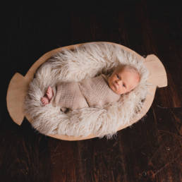 awake newborn baby in wooden trencher bowl filled with faux fur