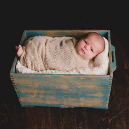newborn baby swaddled in knit blanket in antique wood crate