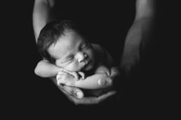 newborn baby in parents interlaced fingers