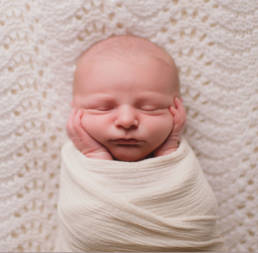swaddled newborn baby with hands on cheeks