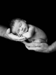 newborn baby with legs folded under body asleep in parent's hands